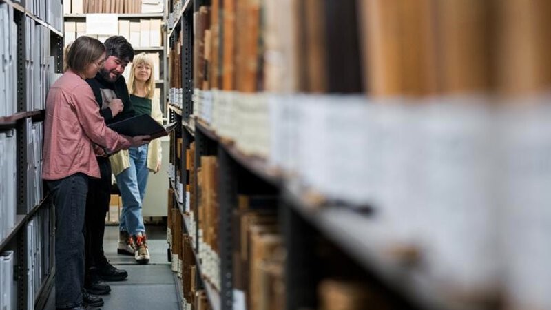 Foto av tre mennesker i et arkivmagasin