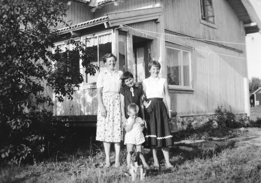 Foto av en voksen, tre barn i ulik alder og en hund, alle foran et bolighus