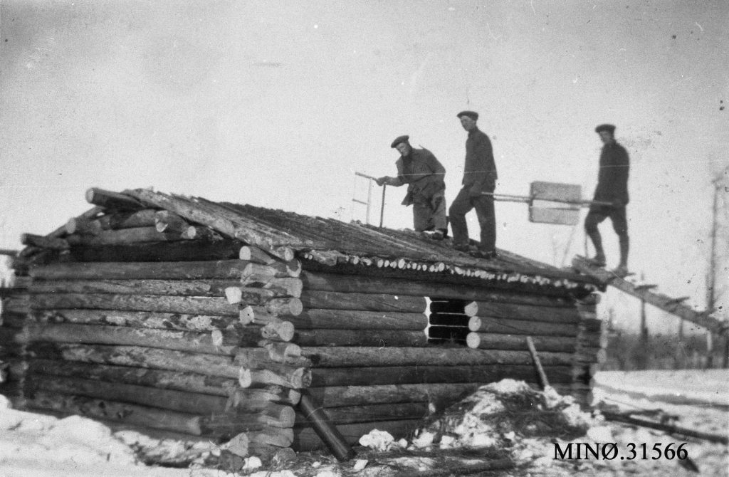 Foto av tre menn på taket av en tømmerhytte