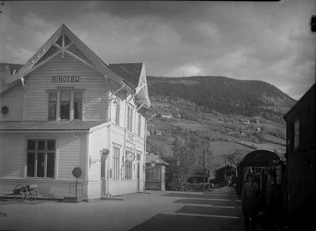 Foto av et hvitt hus med teksten "Ringebu", en perrong og deler av et tog.