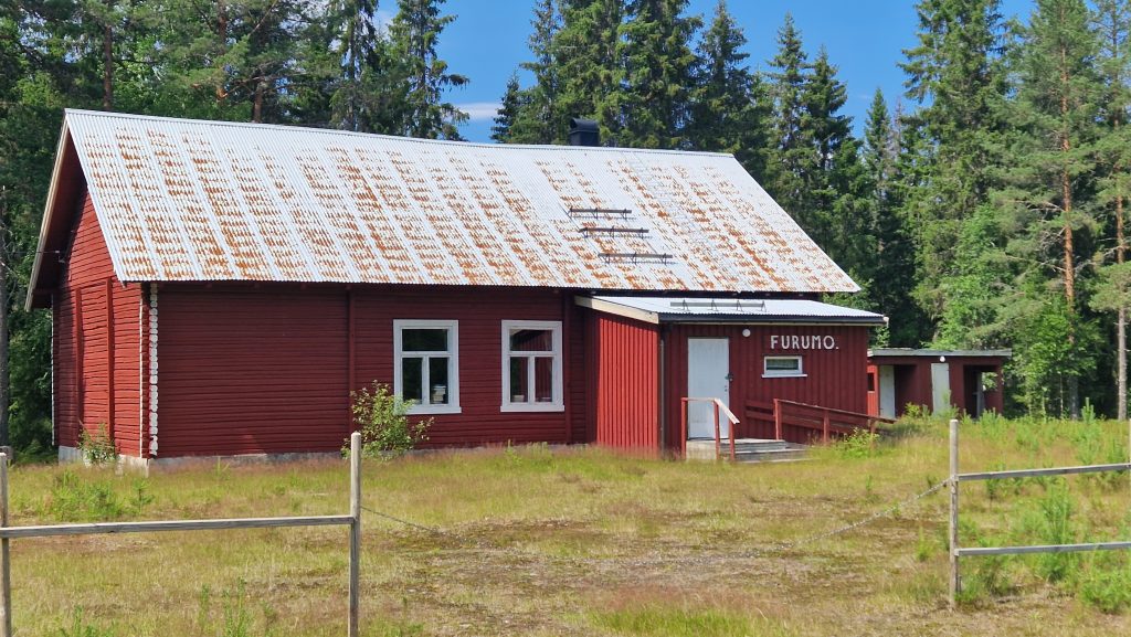 Foto av et eldre rødt hus, med teksten "Furumo" på husveggen ved inngangsdøra.