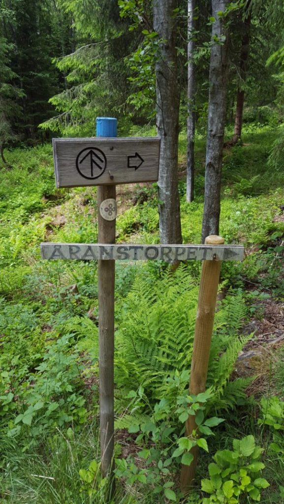Foto av et treskilt i skogen, skiltet har teksten Åranstorpet og en pil mot høyre.