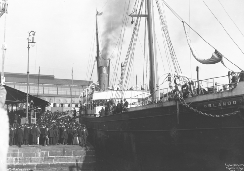 Skipet Orlando forlater kai i 1901. Svart-hvitt foto av et stort skip ved havn, og mange mennesker på skip og havn.