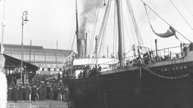 Skipet Orlando forlater kai i 1901. Svart-hvitt foto av et stort skip ved havn, og mange mennesker på skip og havn.